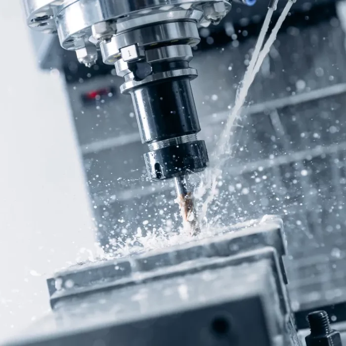 Nahaufnahme einer CNC-Fräsmaschine, die Metall mit einem rotierenden Bohrer schneidet. Kühlmittel spritzt umher und kühlt Werkzeug und Material. Der Hintergrund ist unscharf und fokussiert den Präzisionsbearbeitungsprozess.