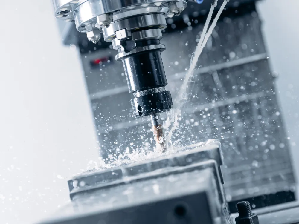 Nahaufnahme einer CNC-Fräsmaschine, die Metall mit einem rotierenden Bohrer schneidet. Kühlmittel spritzt umher und kühlt Werkzeug und Material. Der Hintergrund ist unscharf und fokussiert den Präzisionsbearbeitungsprozess.